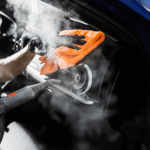 Nettoyage vapeur intérieur voiture: vapeur et chiffon orange désinfectent le tableau de bord noir autour d'une aération.