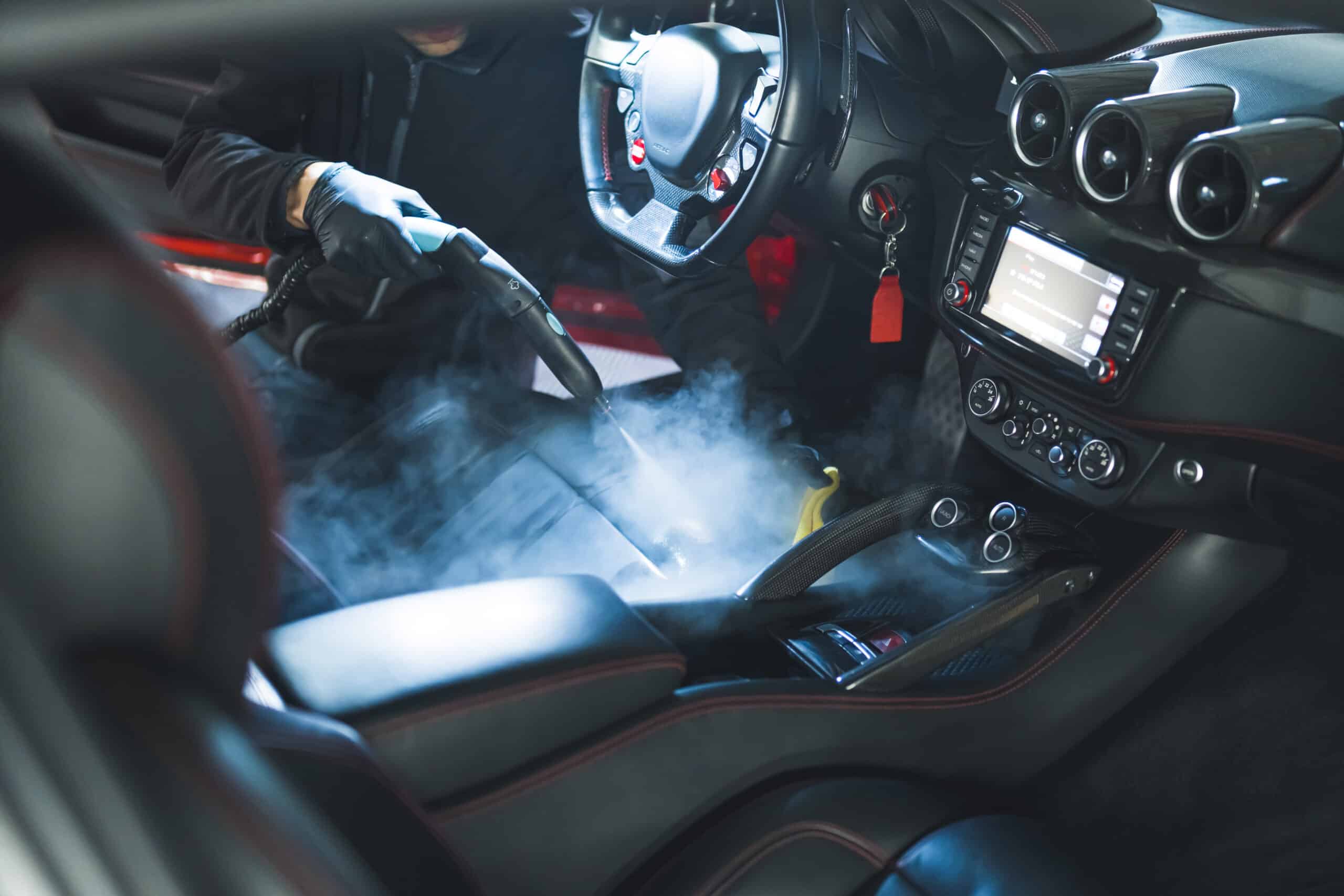 Nettoyage vapeur intérieur voiture luxe, ganté, focalisation sur siège cuir et console centrale carbone. Vapeur visible.